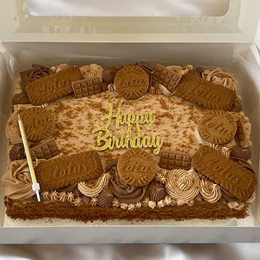 Birthday cake topped with caramel swirls, decorated with Lotus biscuits and a candle in a white box.