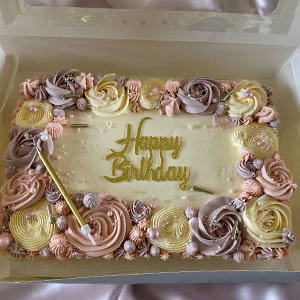 A beautifully decorated birthday cake featuring pastel-colored frosting roses, topped with a golden