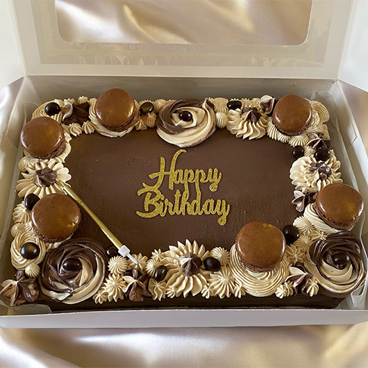 A beautifully decorated chocolate birthday cake in a box, featuring the words