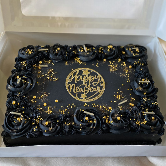 A rectangular black cake decorated with black icing roses and golden sprinkles, featuring the text 