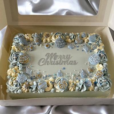 A beautifully decorated Christmas cake with intricate blue and gold icing designs, featuring the message 