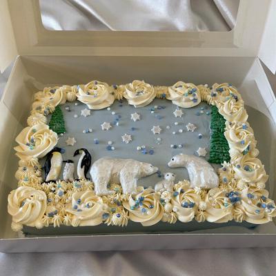 A decorated cake featuring a snowy scene with two penguins and a polar bear surrounded by cream roses and blue embellishments, perfect for themed celebrations.