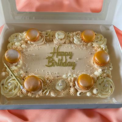 Birthday cake decorated with golden macarons and creamy swirls, featuring the words