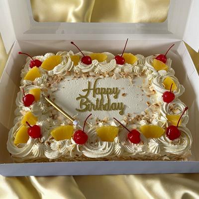 A decorated birthday cake with yellow frosting, cherries, and pineapple pieces arranged around the edges, featuring the text