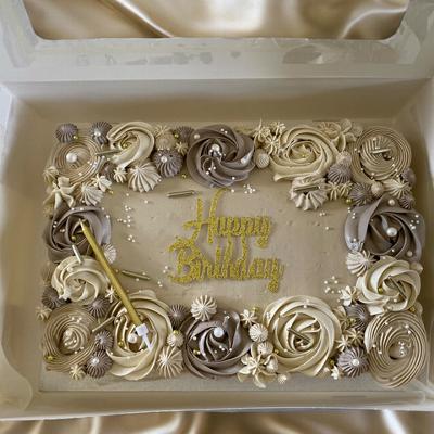 A beautifully decorated birthday cake with intricate floral icing designs in shades of beige and cream, featuring a golden