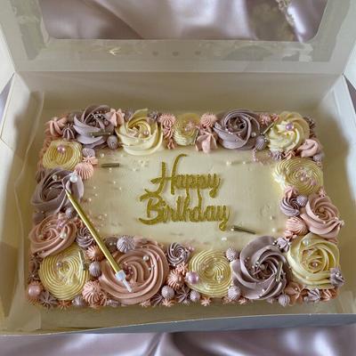 A beautifully decorated birthday cake with pastel-colored frosting roses in pink, purple, and cream, featuring the words