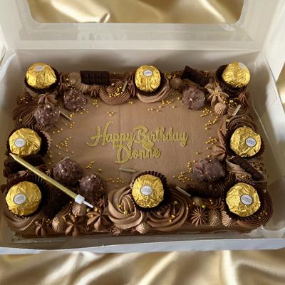 A chocolate birthday cake decorated with golden foil-wrapped chocolates, sprinkles, and the text