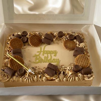 A decorated birthday cake with frosting, cookies, and chocolates, featuring the words